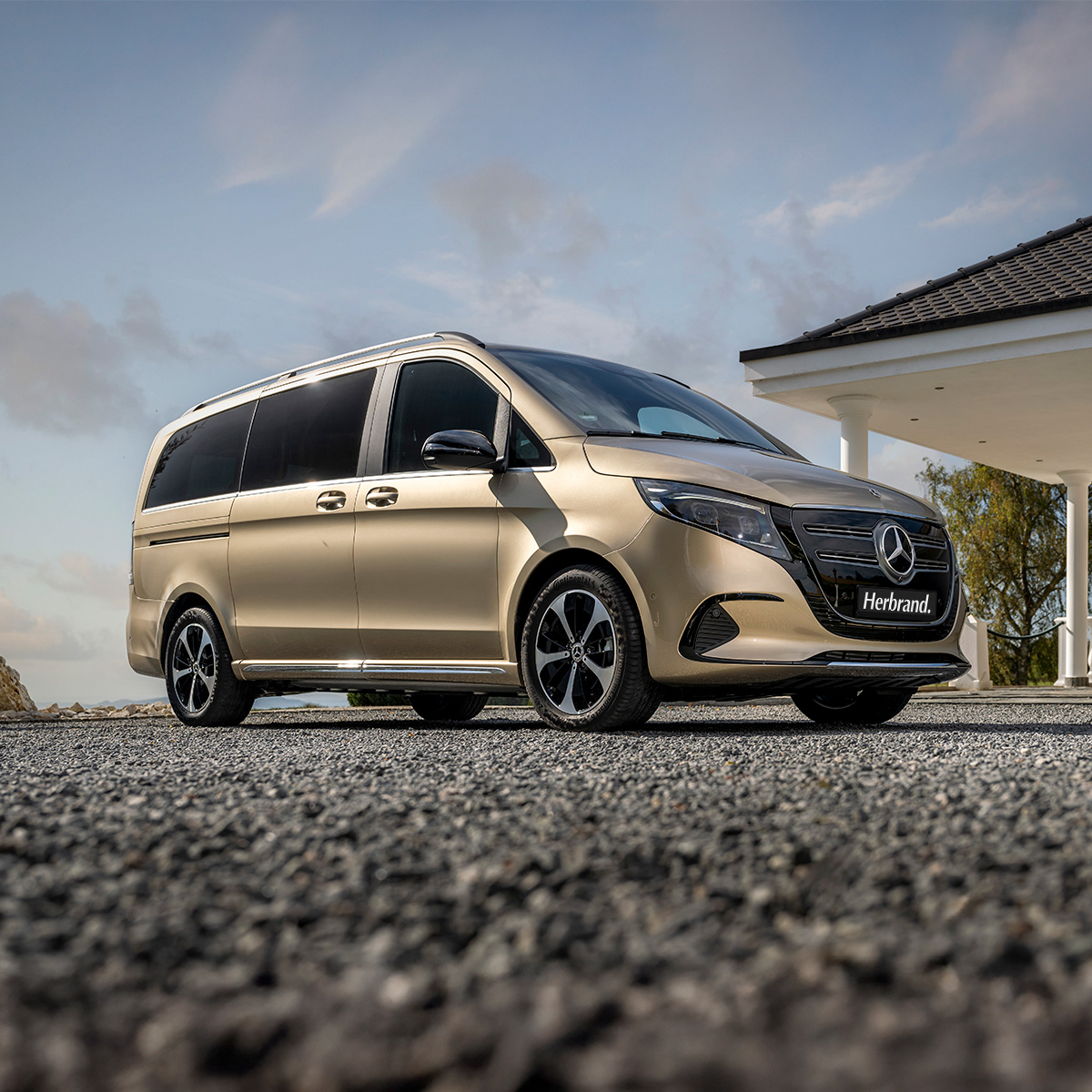 Vollelektrischer EQV in gold steht auf einer Einfahrt vor einem mediterranen Gebäude